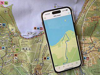 En papperskarta och en mobiltelefon som visar samma plats på kartan.